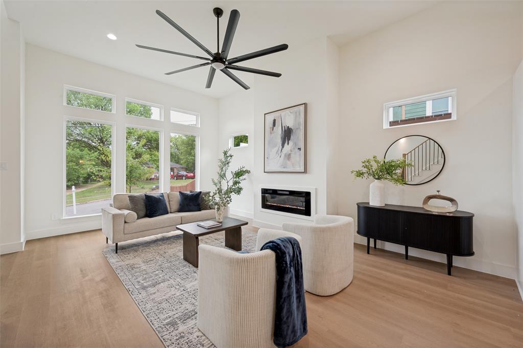 Vaulted ceilings, wood-finish flooring, large multi-pane windows, a linear electric fireplace, and a contemporary ceiling fan