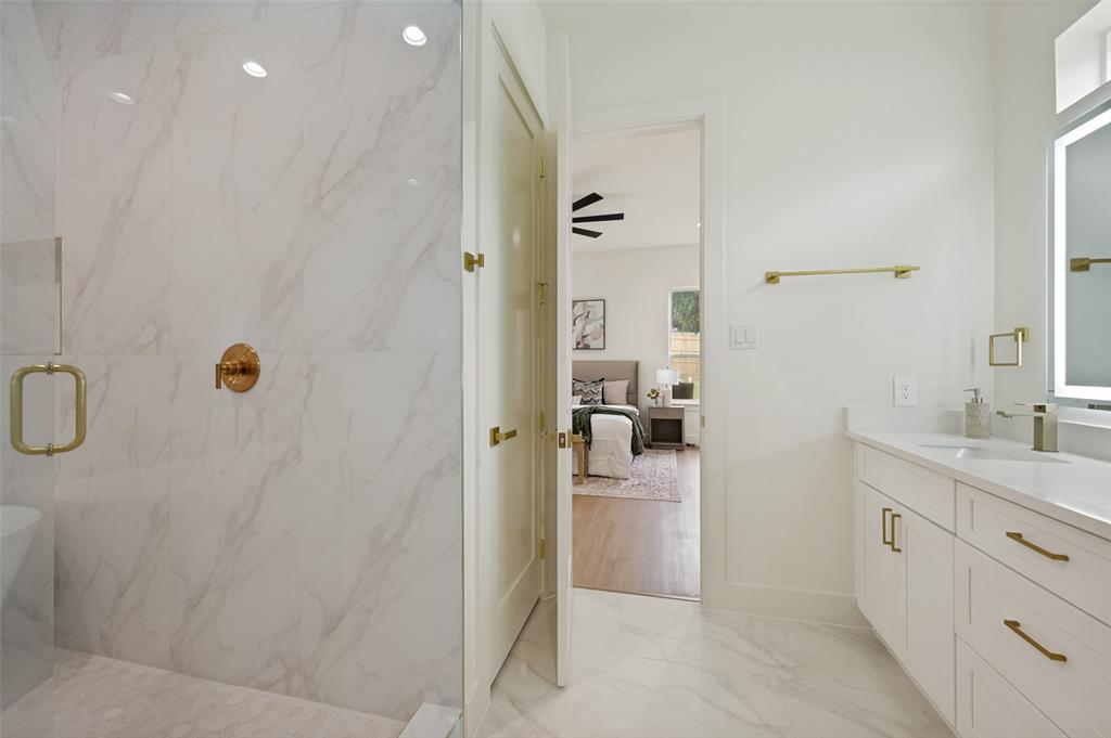 Glass-enclosed shower with gold-tone fixtures and marble-look tile