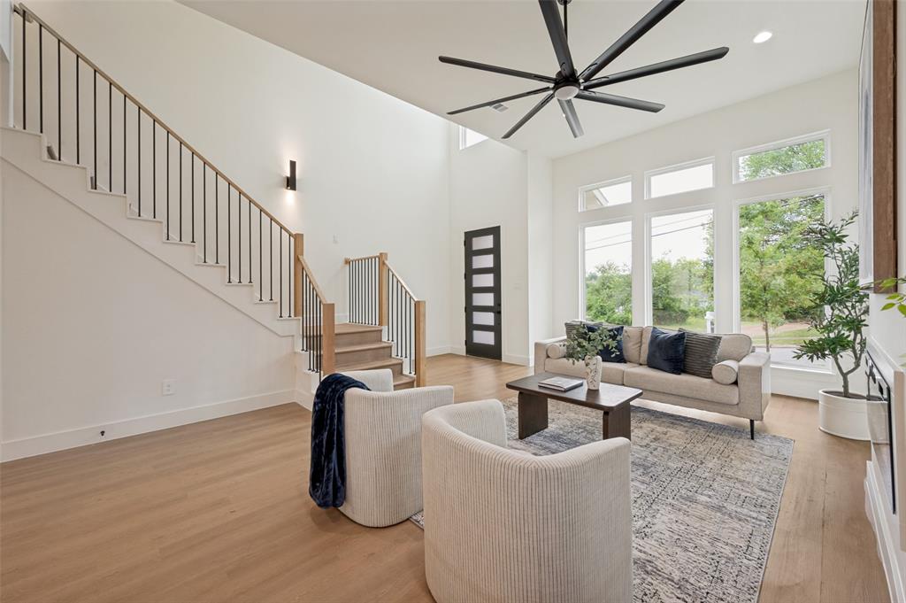 Two-story entry featuring wood-finish flooring, a modern staircase with wood handrails and black metal balusters, a large ceiling fan, and expansive windows