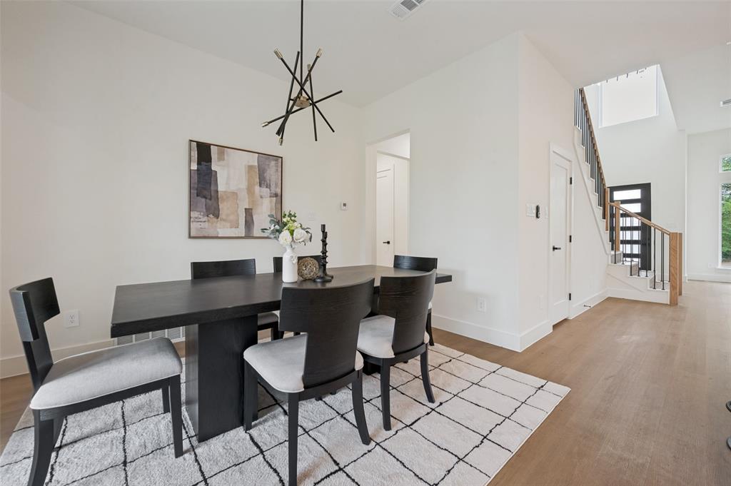 Open-concept living area featuring a modern chandelier, light wood-finish flooring, and a contemporary staircase with wood and metal railing