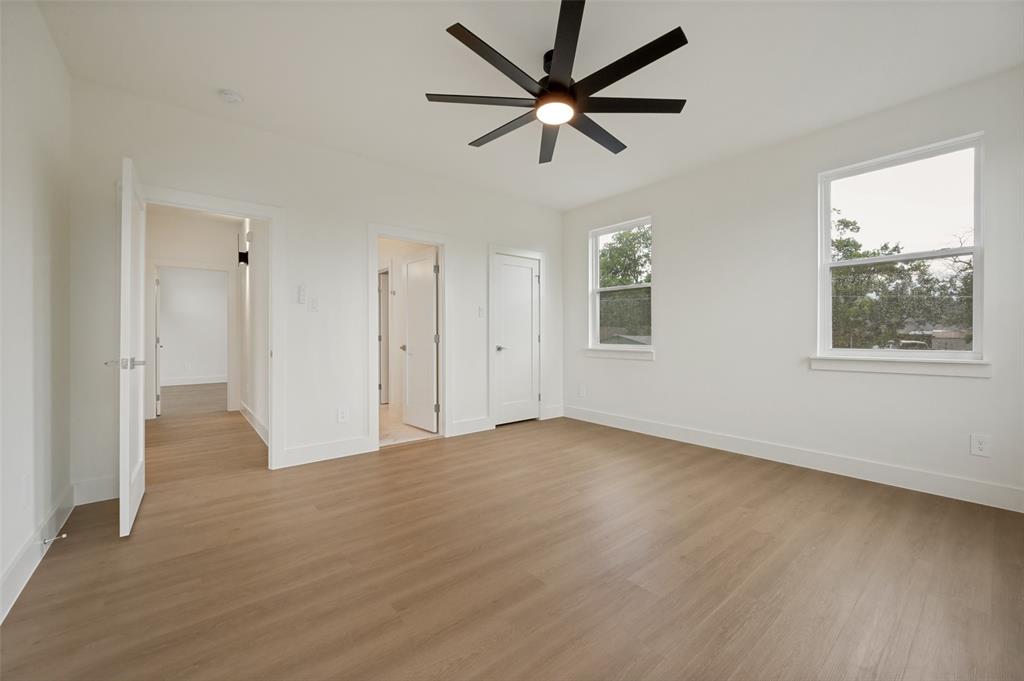 Spacious room featuring light wood-finish flooring, a modern black ceiling fan, and multiple windows