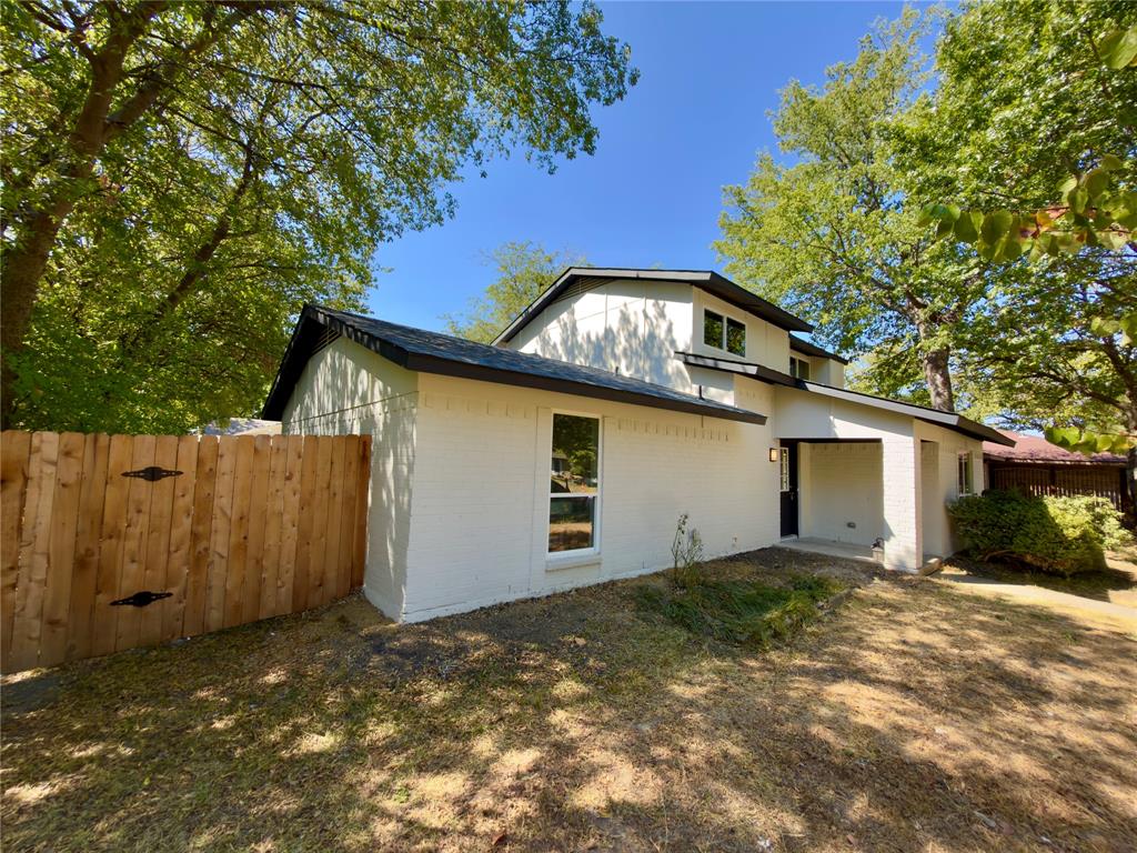 Contemporary exterior featuring white painted brick, a black shingle roof, a wood privacy fence, and a covered entry