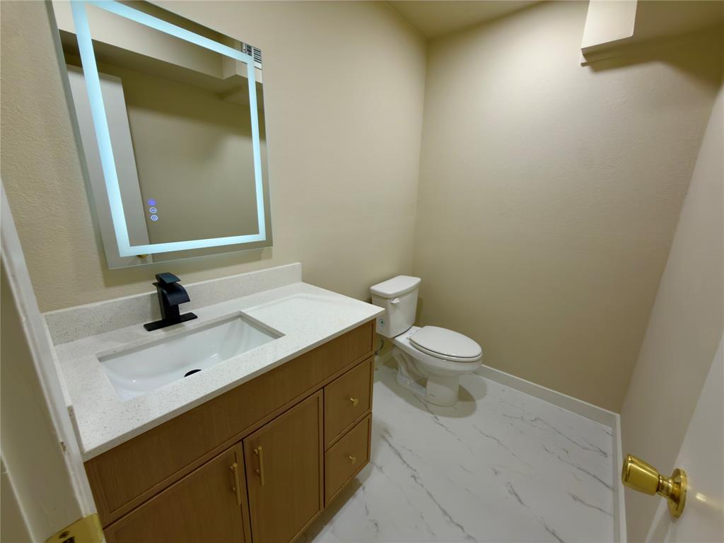 Vanity with integrated sink, modern black faucet, illuminated mirror, and marble-look flooring