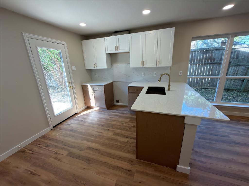 Kitchen featuring an island with a built-in sink, white cabinetry with gold-tone hardware, wood-finish flooring, recessed lighting, and a glass-paneled exterior door
