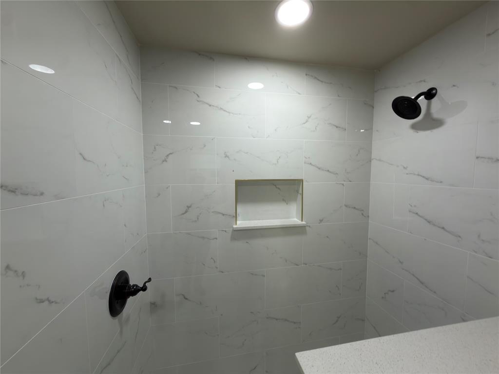 Shower featuring white tile with gray veining, a built-in shower niche, matte black shower fixtures, and recessed lighting