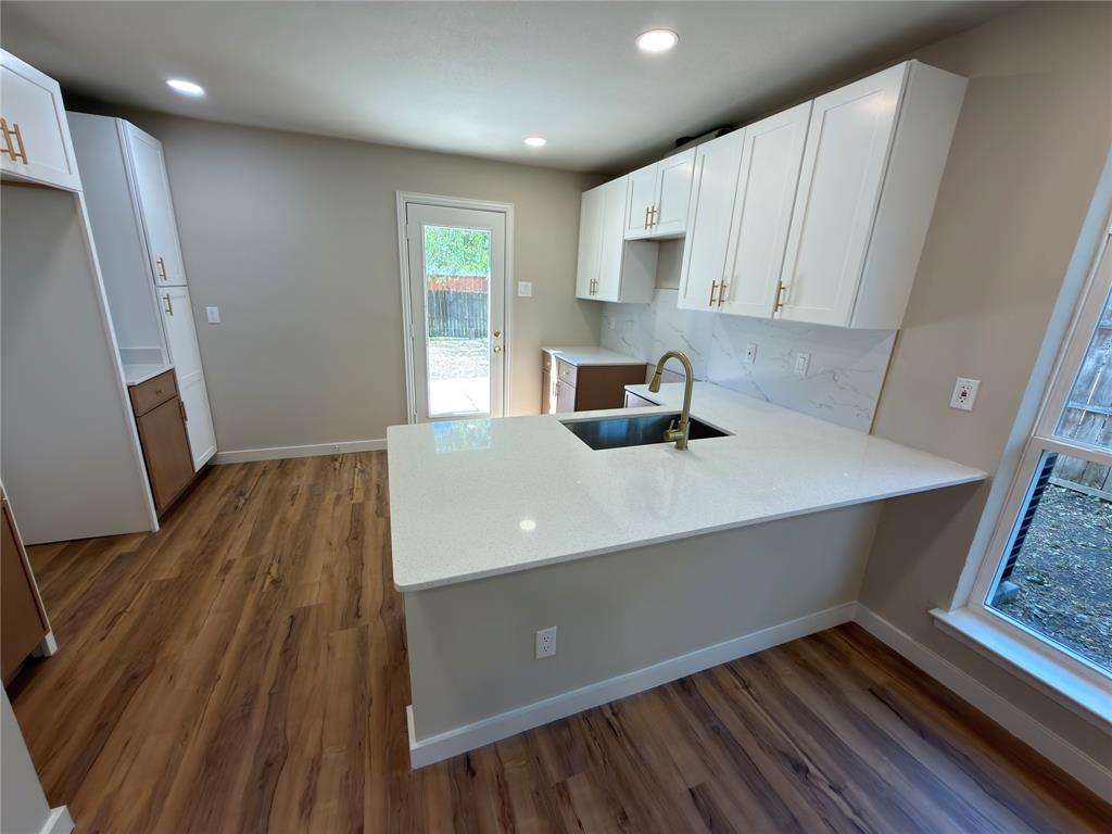 Kitchen featuring white shaker cabinetry, wood-finish flooring, recessed lighting, a kitchen island with an undermount sink, and a full backsplash