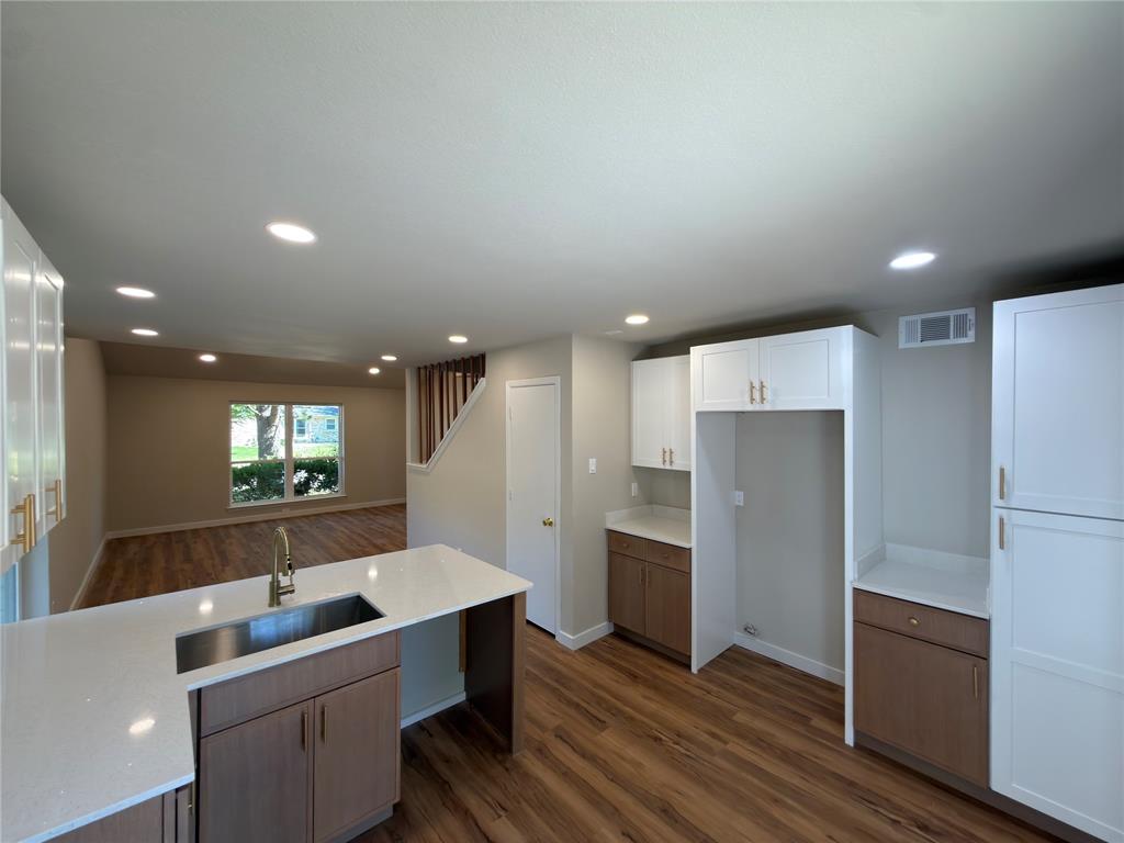 Kitchen featuring white upper cabinetry, wood-finish lower cabinetry, white countertops, and a stainless steel sink with a gooseneck faucet