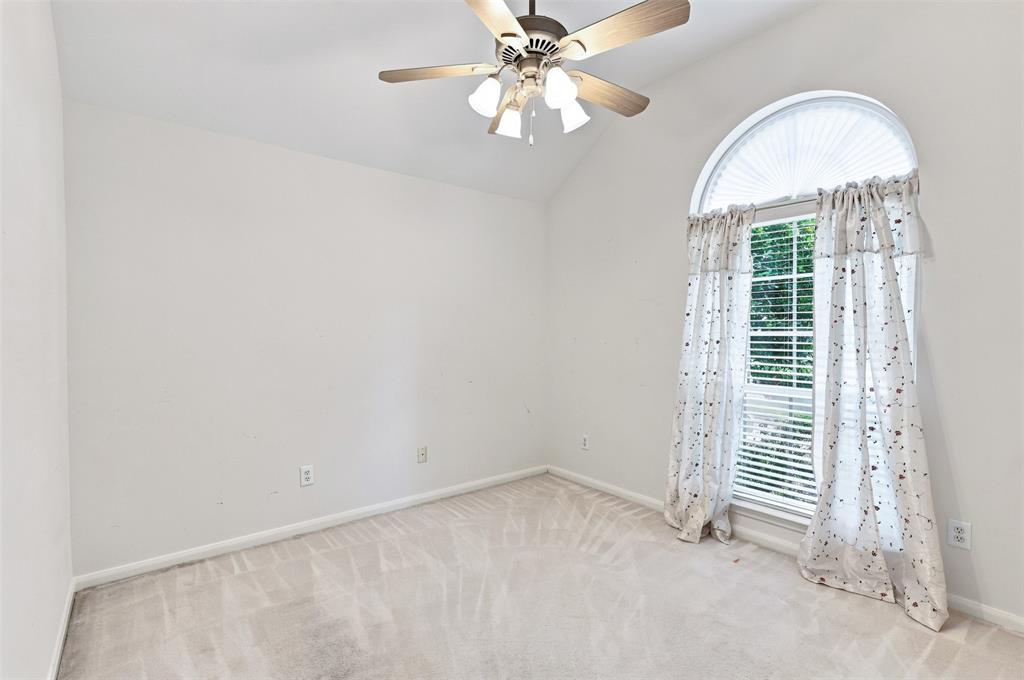 Secondary bedroom with vaulted ceiling with an attached ceiling fan, arched window with horizontal blinds, and neutral carpet flooring.