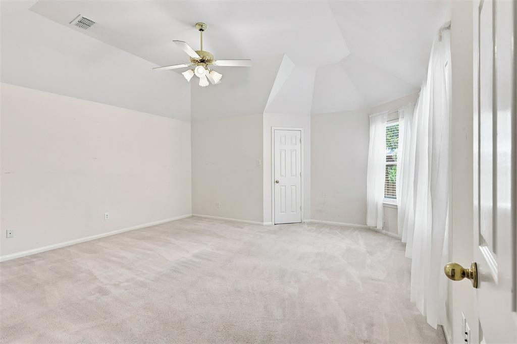 Primary bedroom features vaulted ceilings, carpeted flooring, ceiling fan with integrated lighting, paneled door, and a multi-pane window.