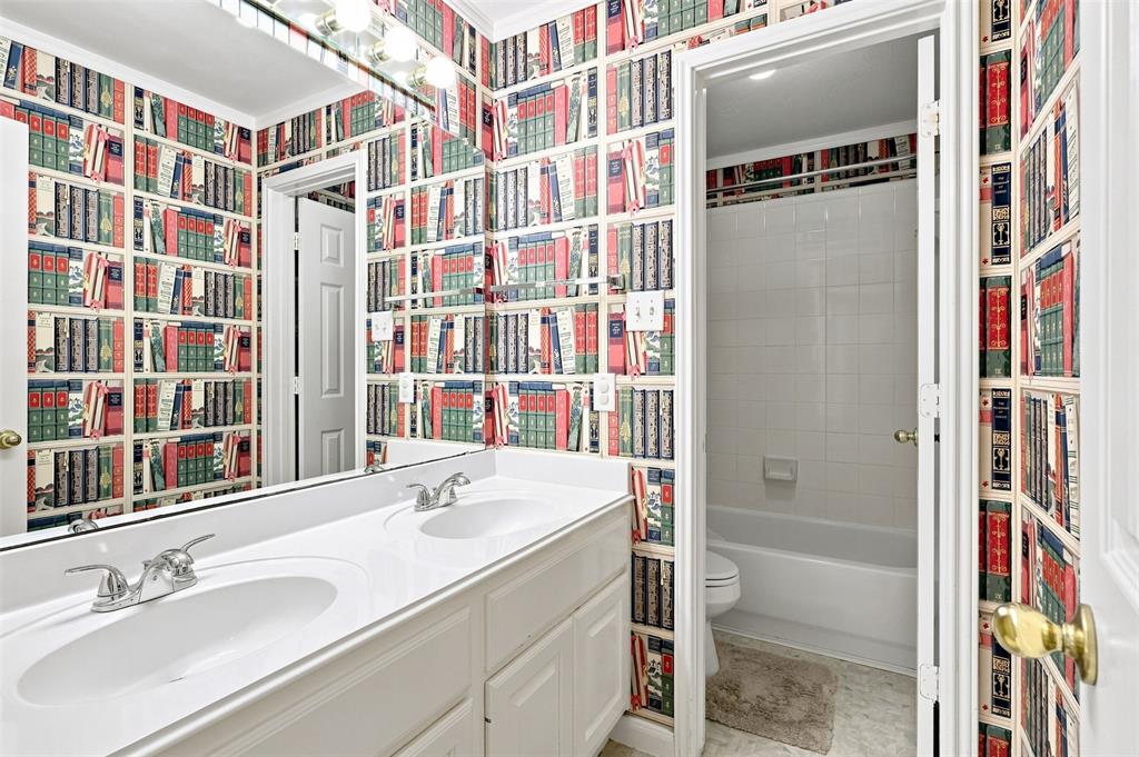 Secondary bathroom with dual sinks and private toilet and shower/tub combo.