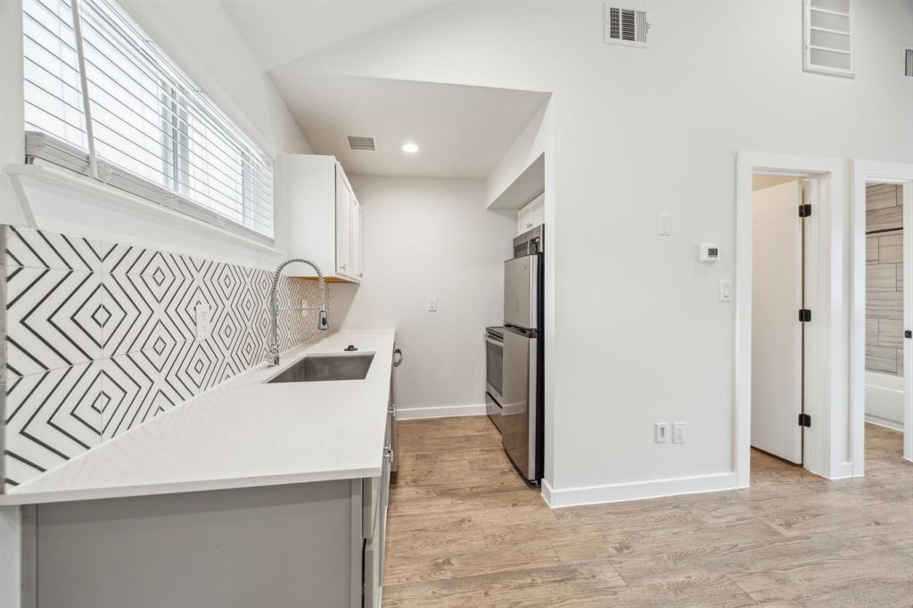 Kitchenette with stainless steel appliances, wood-finish flooring, white cabinetry, geometric tile backsplash, and a deep undermount sink