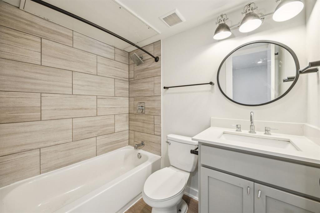 Bathroom featuring a white bathtub, wood-finish wall tiling, a light gray vanity with a white countertop, an undermount sink, and a circular mirror