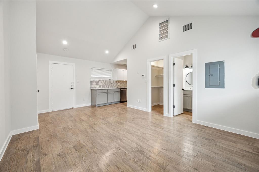 Vaulted ceiling with recessed lighting, wood-finish flooring, kitchen area with a tile backsplash, and a bathroom with a circular mirror