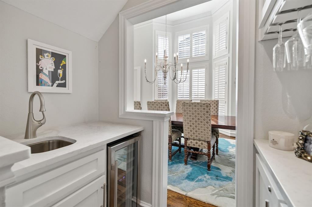 Renovated wet bar with custom cabinetry, wine storage, wine glass display, sink & wine fridge.