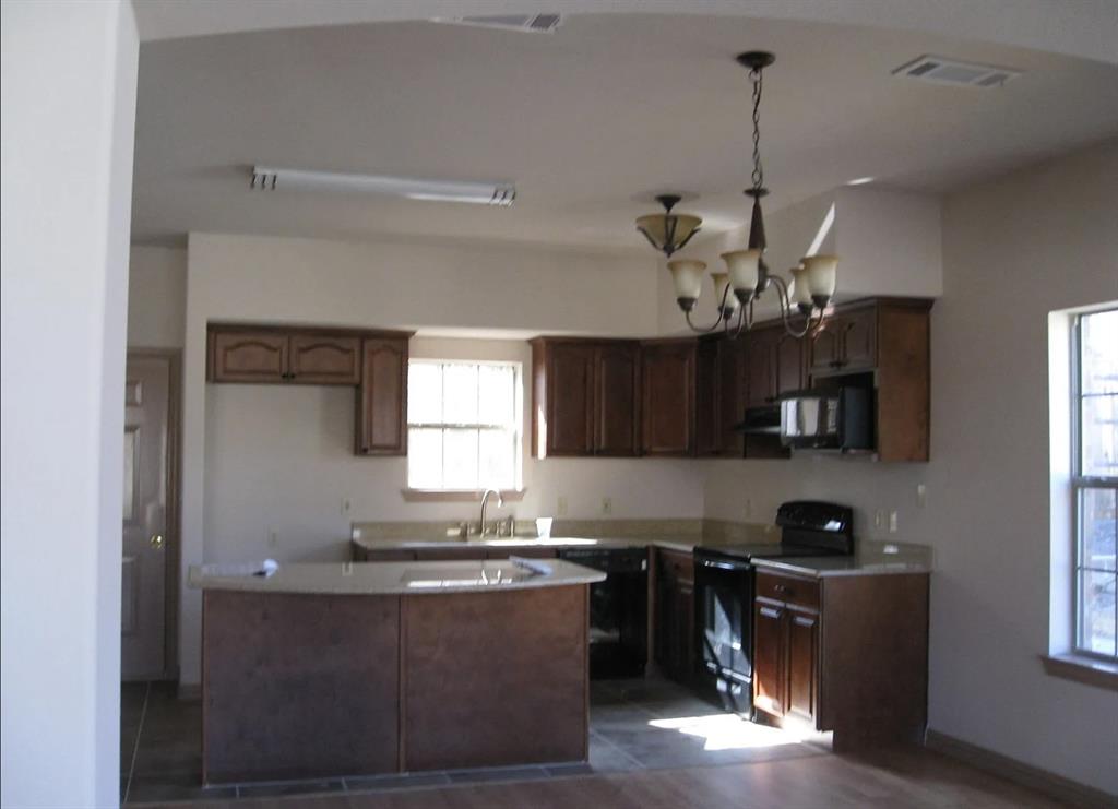 Kitchen featuring dark wood-finish cabinetry, light-toned countertops, a multi-light chandelier, and integrated appliances Kitchen featuring dark wood-finish cabinetry, light-toned countertops, a multi-light chandelier, and integrated appliances