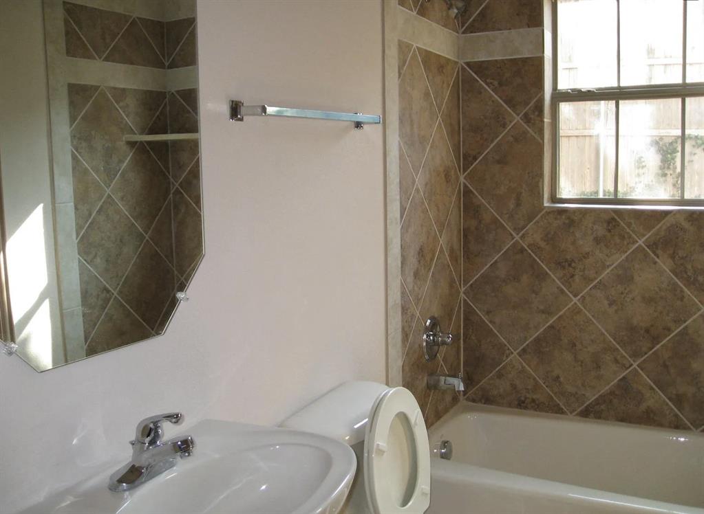 Bathroom featuring a ceramic tile shower surround, bathtub with shower fixture, wall-mounted sink, and an octagonal mirror Bathroom featuring a ceramic tile shower surround, bathtub with shower fixture, wall-mounted sink, and an octagonal mirror