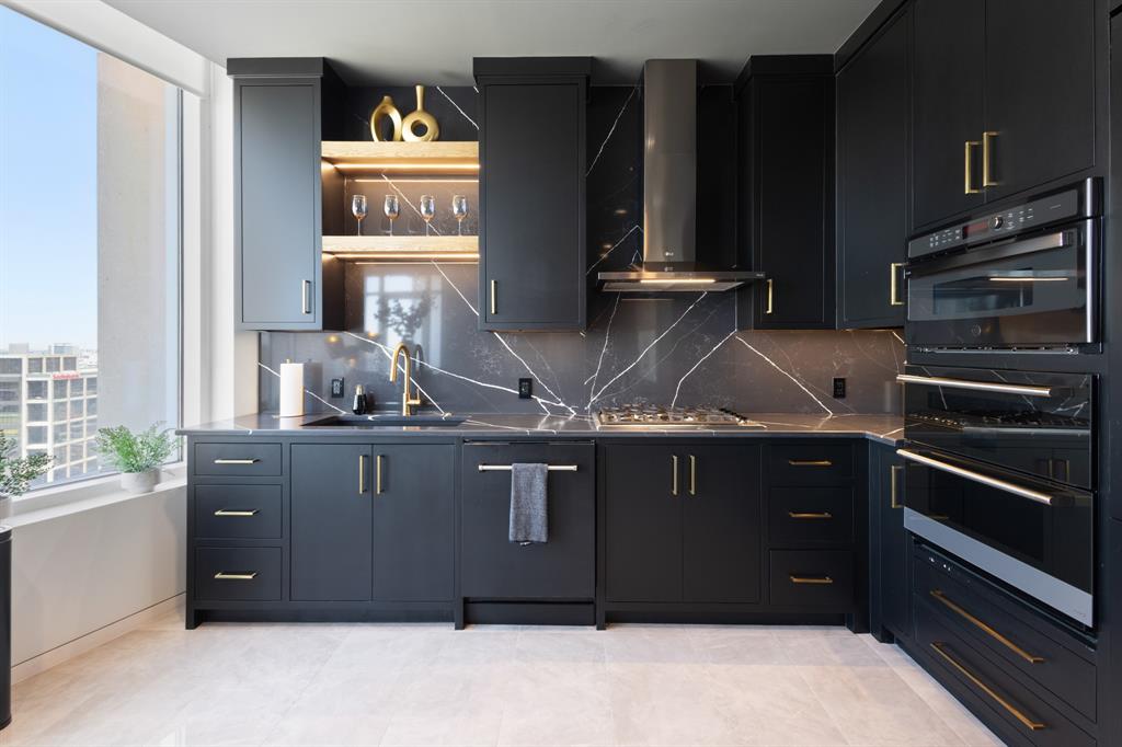 Modern kitchen featuring black cabinetry with gold-tone hardware, a dark marble-patterned backsplash, and a built-in oven and microwave Modern kitchen featuring black cabinetry with gold-tone hardware, a dark marble-patterned backsplash, and a built-in oven and microwave