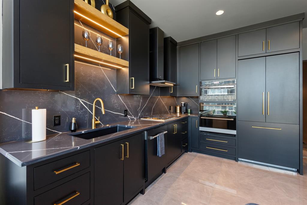Sleek kitchen featuring dark cabinetry, gold-tone hardware, integrated appliances, and a dramatic veined countertop and backsplash Sleek kitchen featuring dark cabinetry, gold-tone hardware, integrated appliances, and a dramatic veined countertop and backsplash