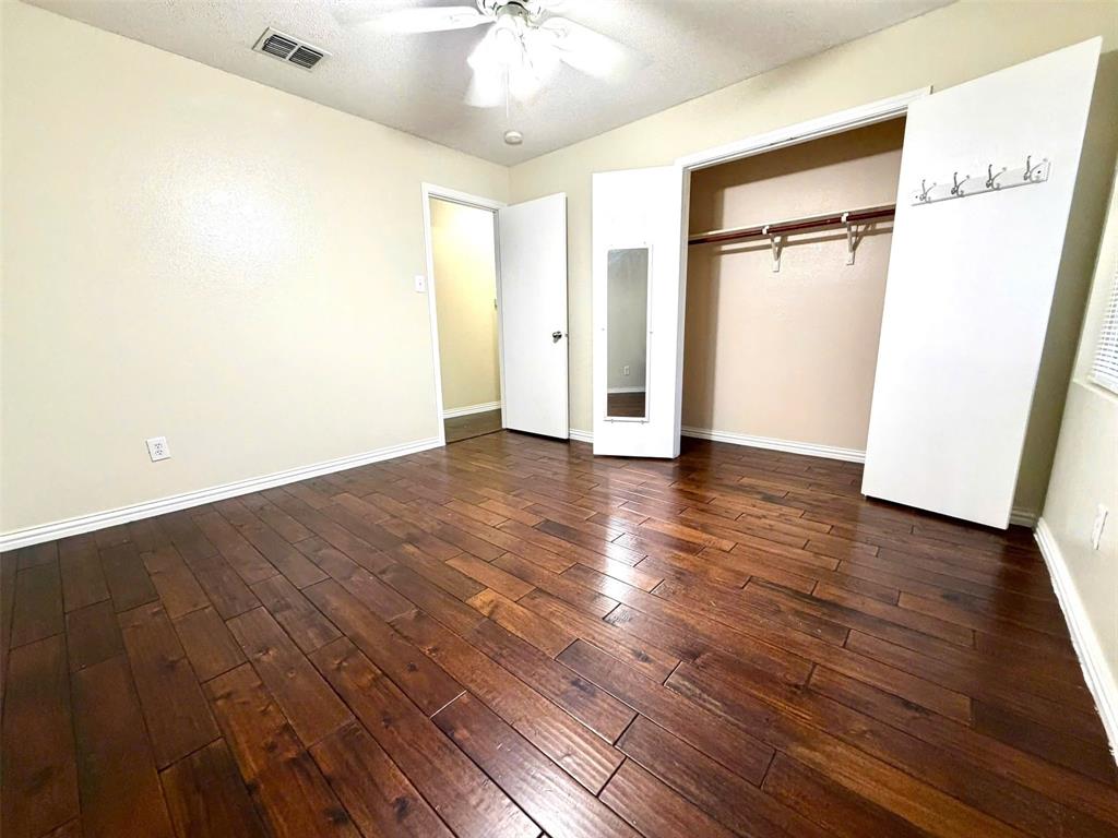 Rich wood-finish flooring, ceiling fan, built-in closet with hanging rod, and light-toned walls