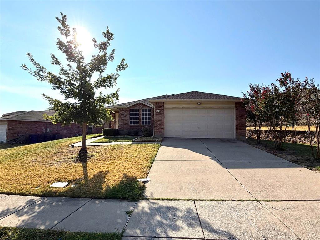 Brick exterior with a gabled roof, an attached two-car garage, a concrete driveway, and a mature tree