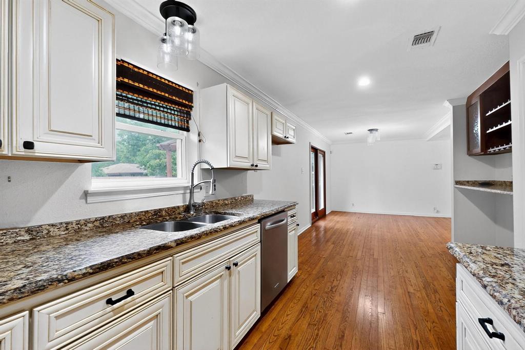 Kitchen with dishwasher, ornamental molding, wood finished floors, dark stone countertops, and white cabinets