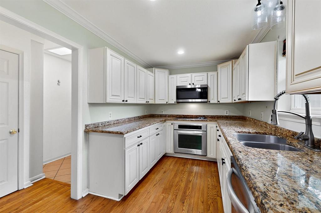 Kitchen with appliances with stainless steel finishes, white cabinetry, crown molding, stone counters, and light wood-style floors Kitchen with appliances with stainless steel finishes, white cabinetry, crown molding, stone counters, and light wood-style floors