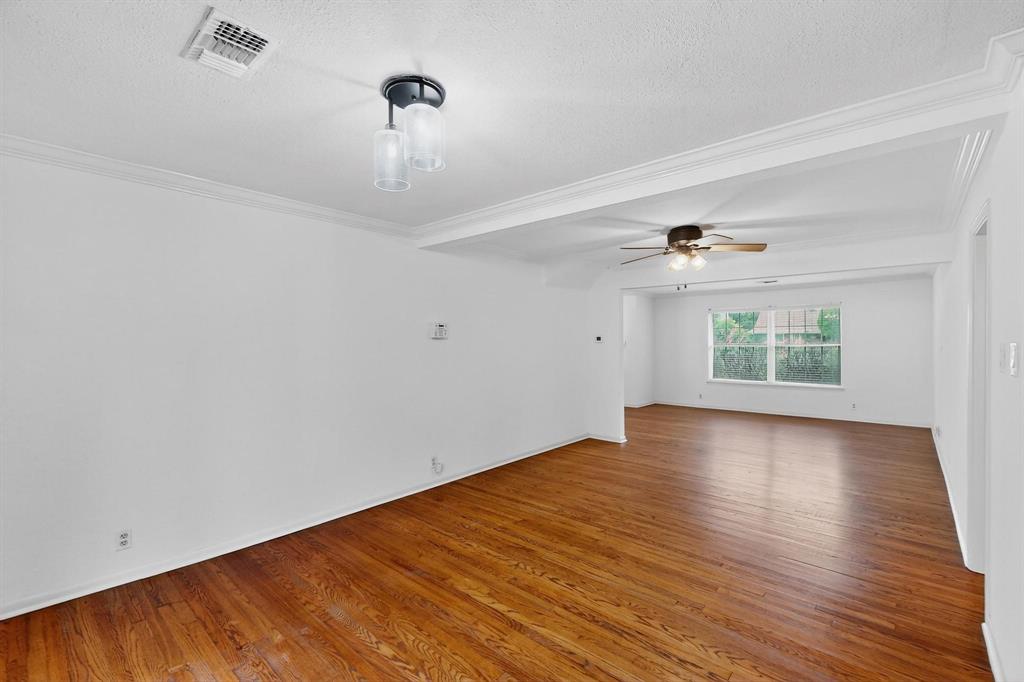 Empty room with wood finished floors, a textured ceiling, a ceiling fan, and crown molding Empty room with wood finished floors, a textured ceiling, a ceiling fan, and crown molding