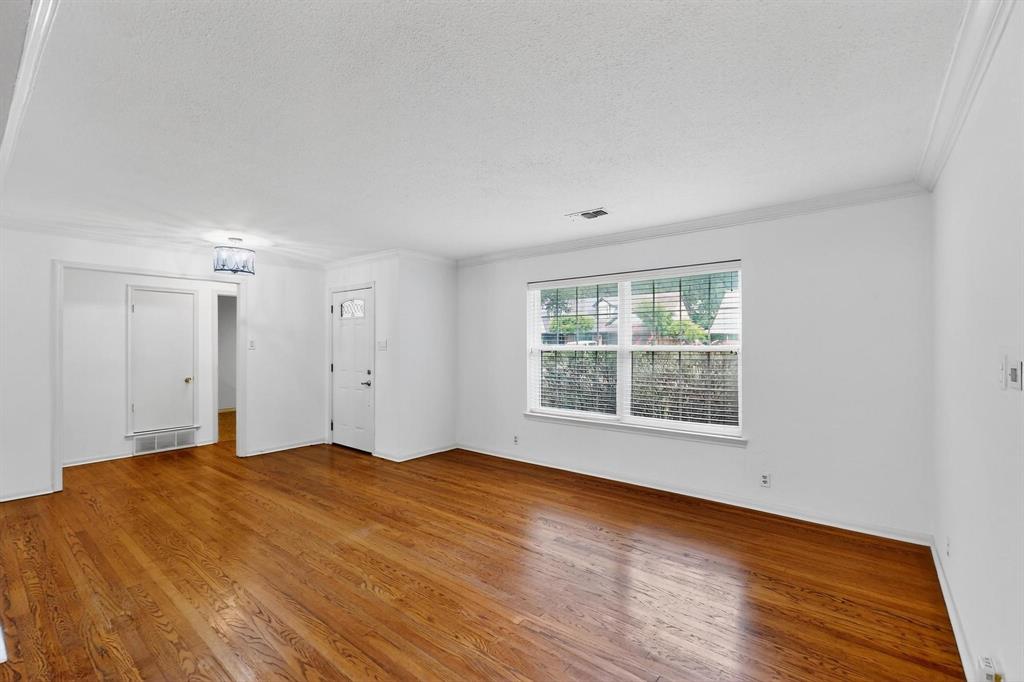Empty room featuring a textured ceiling, wood finished floors, and ornamental molding Empty room featuring a textured ceiling, wood finished floors, and ornamental molding