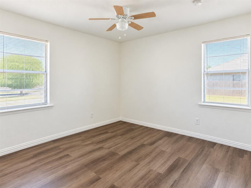Light-filled room featuring two windows, wood-finish flooring, a ceiling fan, and white walls