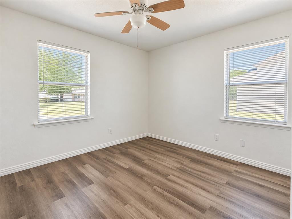 Wood-finish flooring, white walls, two windows with blinds, and a ceiling fan with integrated lighting