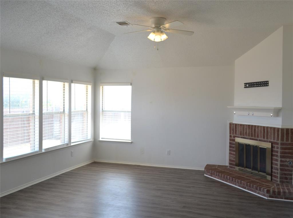 Vaulted ceiling with ceiling fan, multiple windows with blinds, wood-finish flooring, and a brick fireplace with a mantel