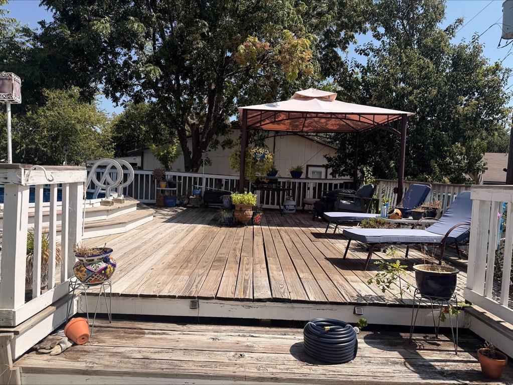 Expansive wood-plank deck with white railings, featuring a built-in pool, and shaded by a gazebo