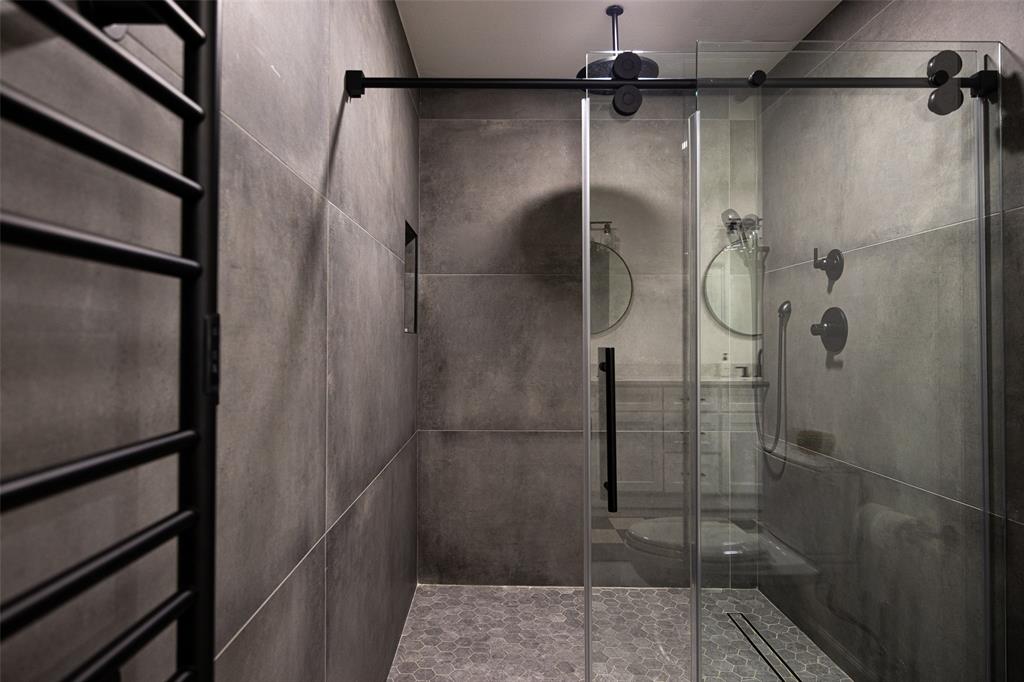 Shower enclosure with sliding glass door, matte black fixtures, full-height wall tiling, and hexagonal floor tiling