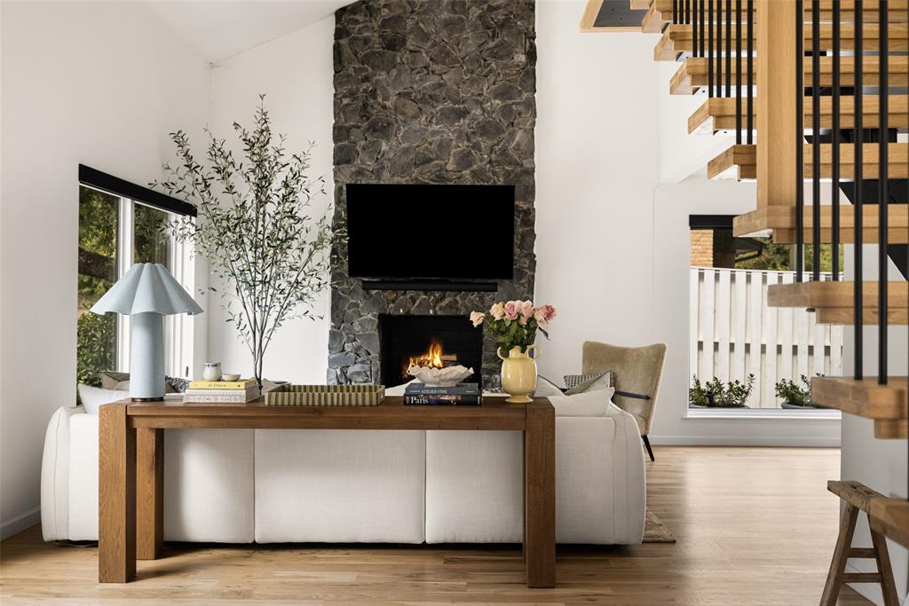Stone-clad fireplace with built-in hearth, wood-finish flooring, white walls, and a modern open-tread staircase with wood and metal railings