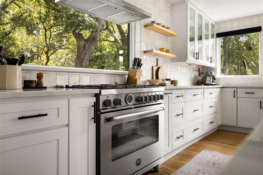 Stainless steel range, white shaker-style cabinetry, light-toned countertops, white subway tile backsplash, and light wood-finish flooring
