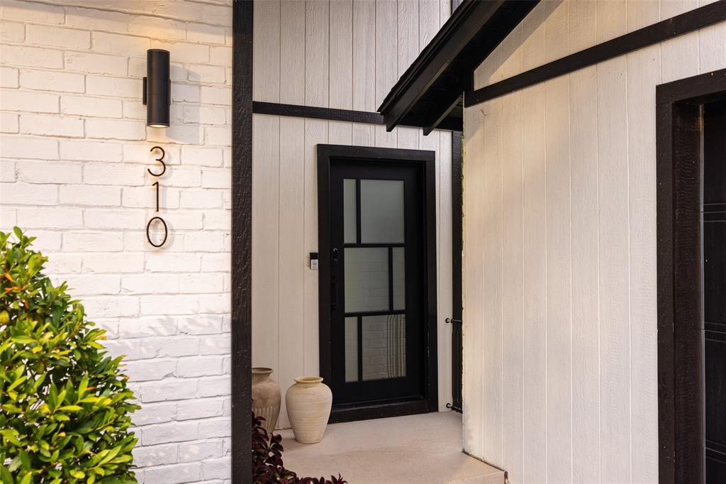 White painted brick facade with a black cylindrical outdoor light fixture, contrasting black window trim, and a black paneled door with frosted glass inserts