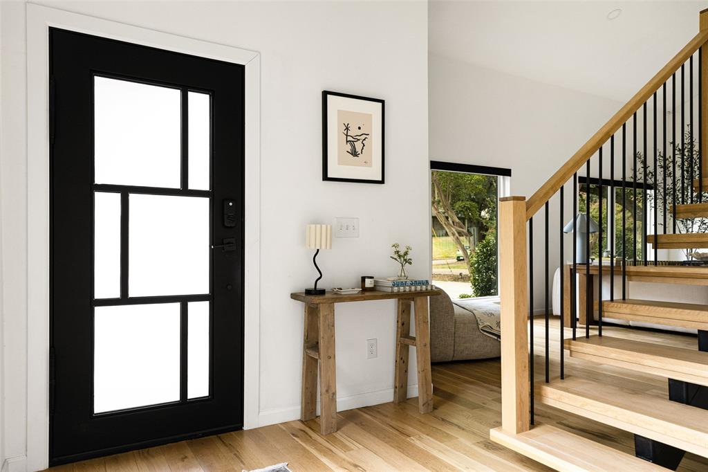 Front entry with a contemporary black door featuring multiple window panes, light wood-finish flooring, a modern open-tread staircase with wood newel posts and handrail, and black metal balusters