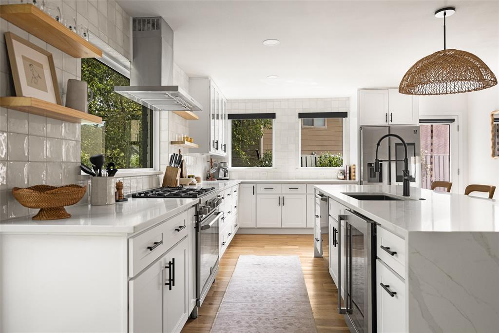 Kitchen featuring white cabinetry, light-toned wood-finish flooring, a stainless steel range hood, stone countertops, and a center island with an integrated beverage cooler