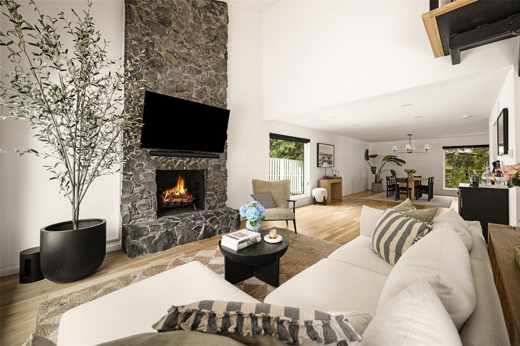 Vaulted ceilings with recessed lighting, stone-finish fireplace, wood-finish flooring, and large windows