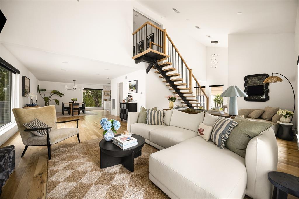 Open-concept living area with wood-finish flooring, a contemporary staircase featuring black spindles and wood handrails, and large windows providing abundant light