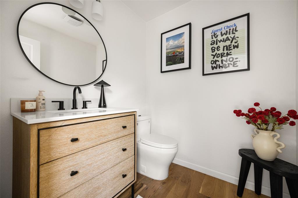 Light wood-finish flooring, a white vanity countertop, black-framed oval mirror, and a modern two-light vanity fixture