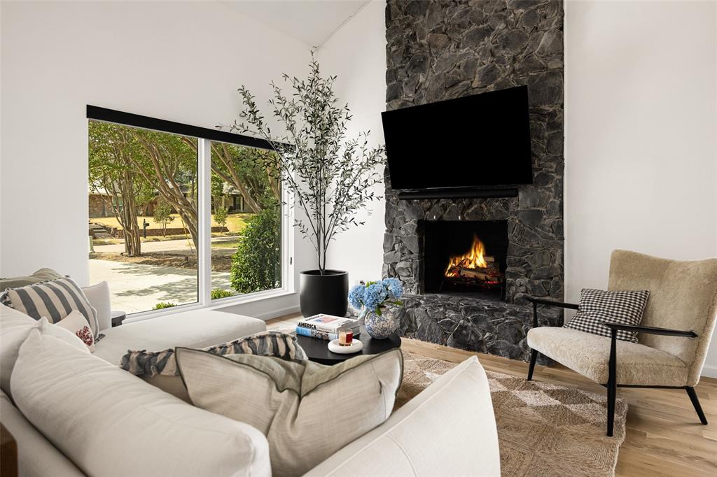 Expansive floor-to-ceiling windows, stone-clad fireplace with hearth, and light wood-finish flooring