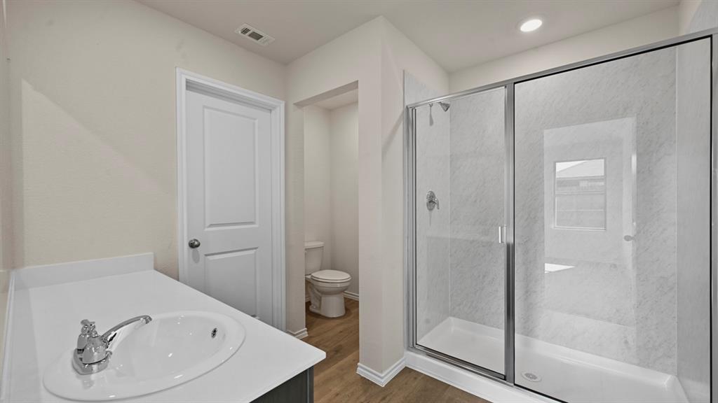 Vanity with an integrated sink, polished chrome faucet, wood-finish flooring, and a glass-enclosed shower with a chrome showerhead