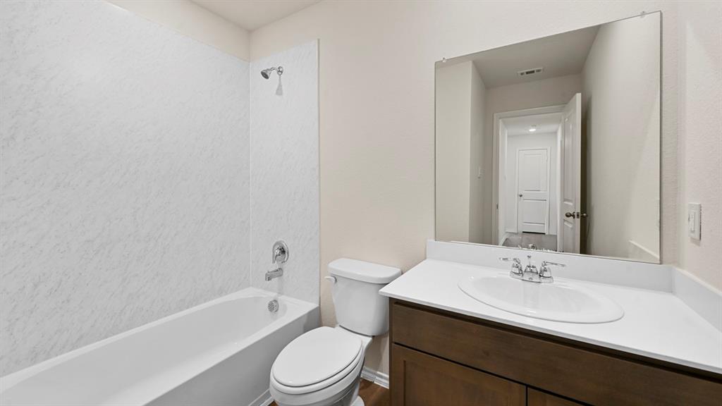 White tub and shower combination with chrome fixtures, a wood-finish vanity with an integrated sink, and an expansive wall mirror