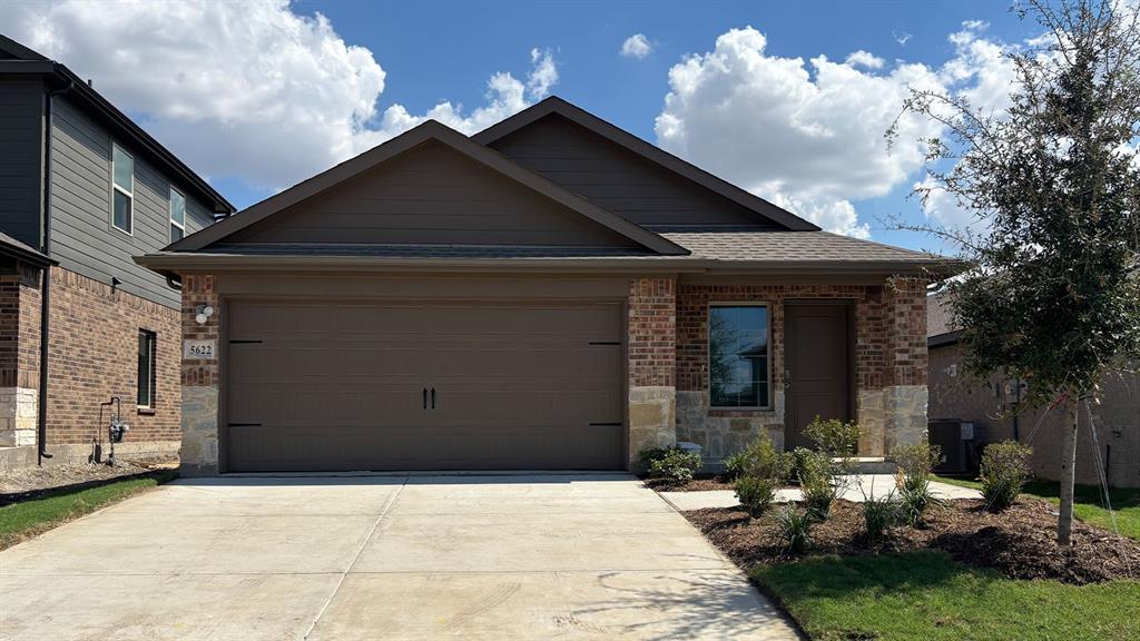 Brick and stone exterior with a two-car garage, front landscaping, and a concrete driveway