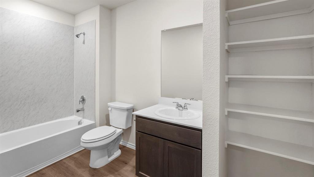 Contemporary bathroom featuring a white tub with a textured surround, a dark wood-finish vanity with a white countertop and integrated sink, a wall-mounted mirror, and built-in shelving Contemporary bathroom featuring a white tub with a textured surround, a dark wood-finish vanity with a white countertop and integrated sink, a wall-mounted mirror, and built-in shelving