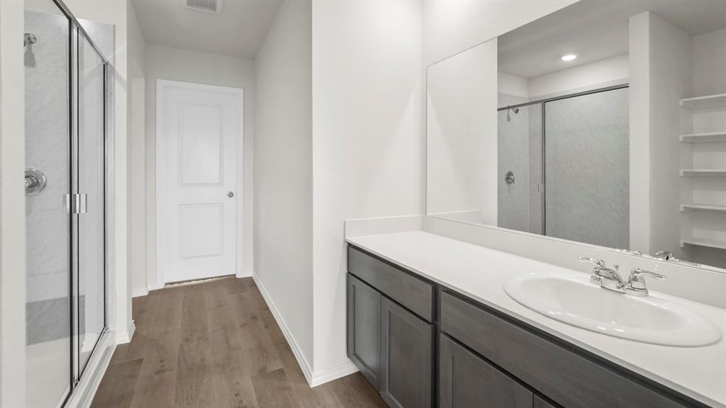 Contemporary bathroom featuring a glass-enclosed shower with subway tile, wood-finish flooring, a white vanity with gray cabinetry, a quartz-finish countertop, and a large wall-mounted mirror Contemporary bathroom featuring a glass-enclosed shower with subway tile, wood-finish flooring, a white vanity with gray cabinetry, a quartz-finish countertop, and a large wall-mounted mirror