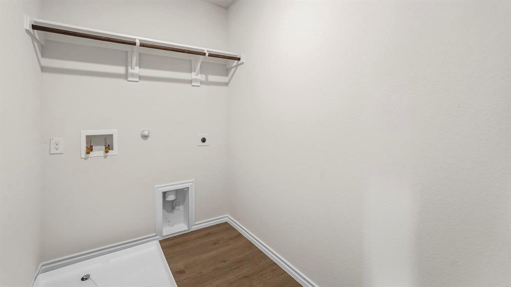 Laundry area with wood-finish flooring, white baseboards, a built-in shelf with hanging rod, and washer/dryer hookups