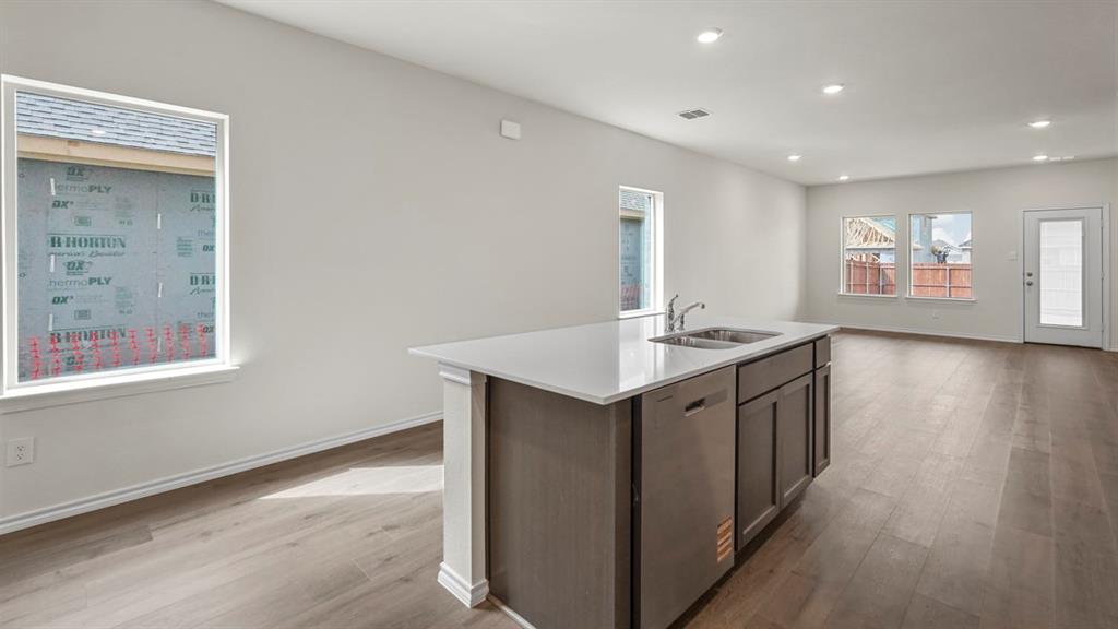 Open-concept living area with wood-finish flooring, recessed lighting, and a kitchen island featuring a double sink, stainless steel dishwasher, and cabinet storage