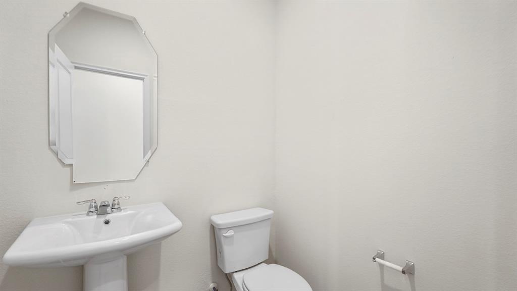 White pedestal sink with chrome faucet hardware, octagonal frameless mirror, and a ceramic toilet